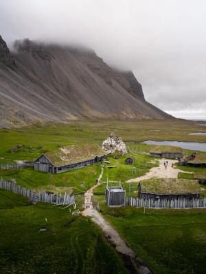 an aerial view of a small village in the middle of a grassy field with a mountain in the background at abandoned viking village in Iceland..