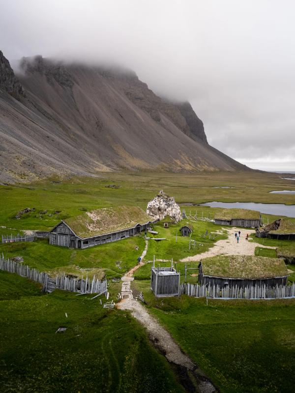 an aerial view of a small village in the middle of a grassy field with a mountain in the background at abandoned viking village in Iceland..
