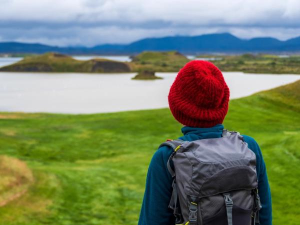 una persona con una mochila y un sombrero rojo está mirando un lago.