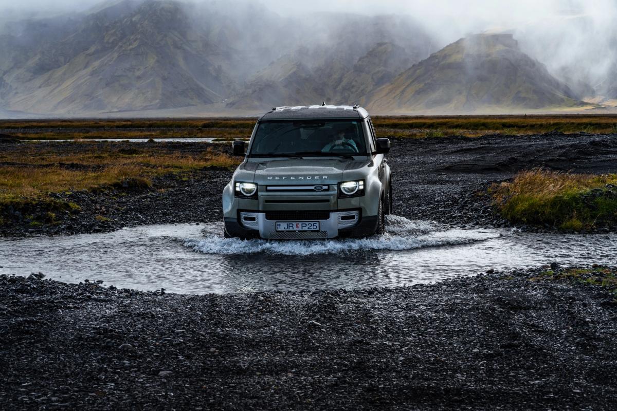 Land Rover Defender de alquiler cruzando un río cerca de unas montañas cubiertas de niebla en Islandia, disponible en Go Car Rental