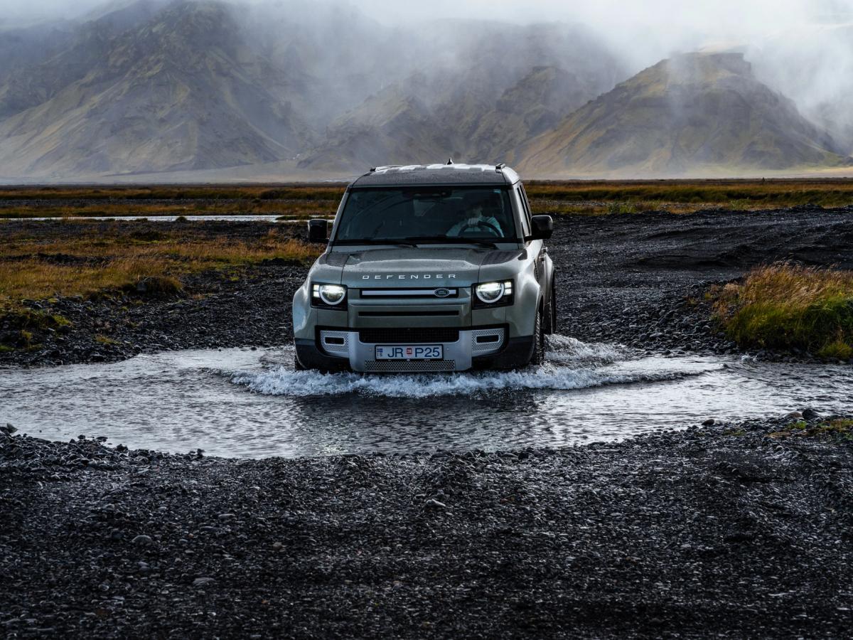 Defensor cruzando un río Land Rover Defender de alquiler cruzando un río cerca de unas montañas cubiertas de niebla en Islandia, disponible en Go Car Rental