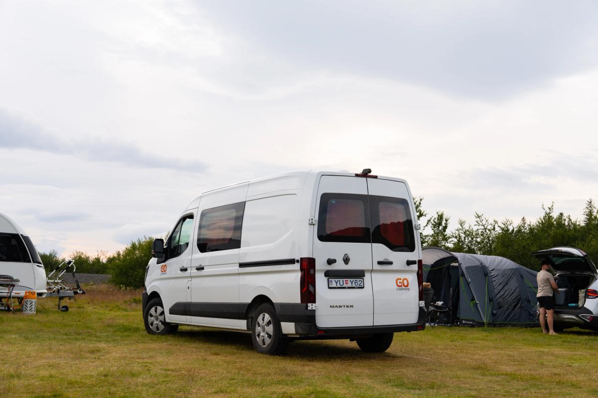A 5 person large camper from the rear at a campsite beside tents, self drive Iceland
