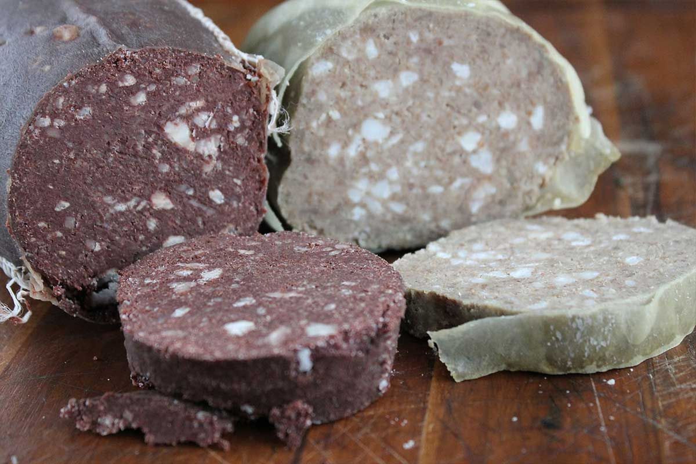 Slices of dark blood pudding and light white pudding on a wooden board.