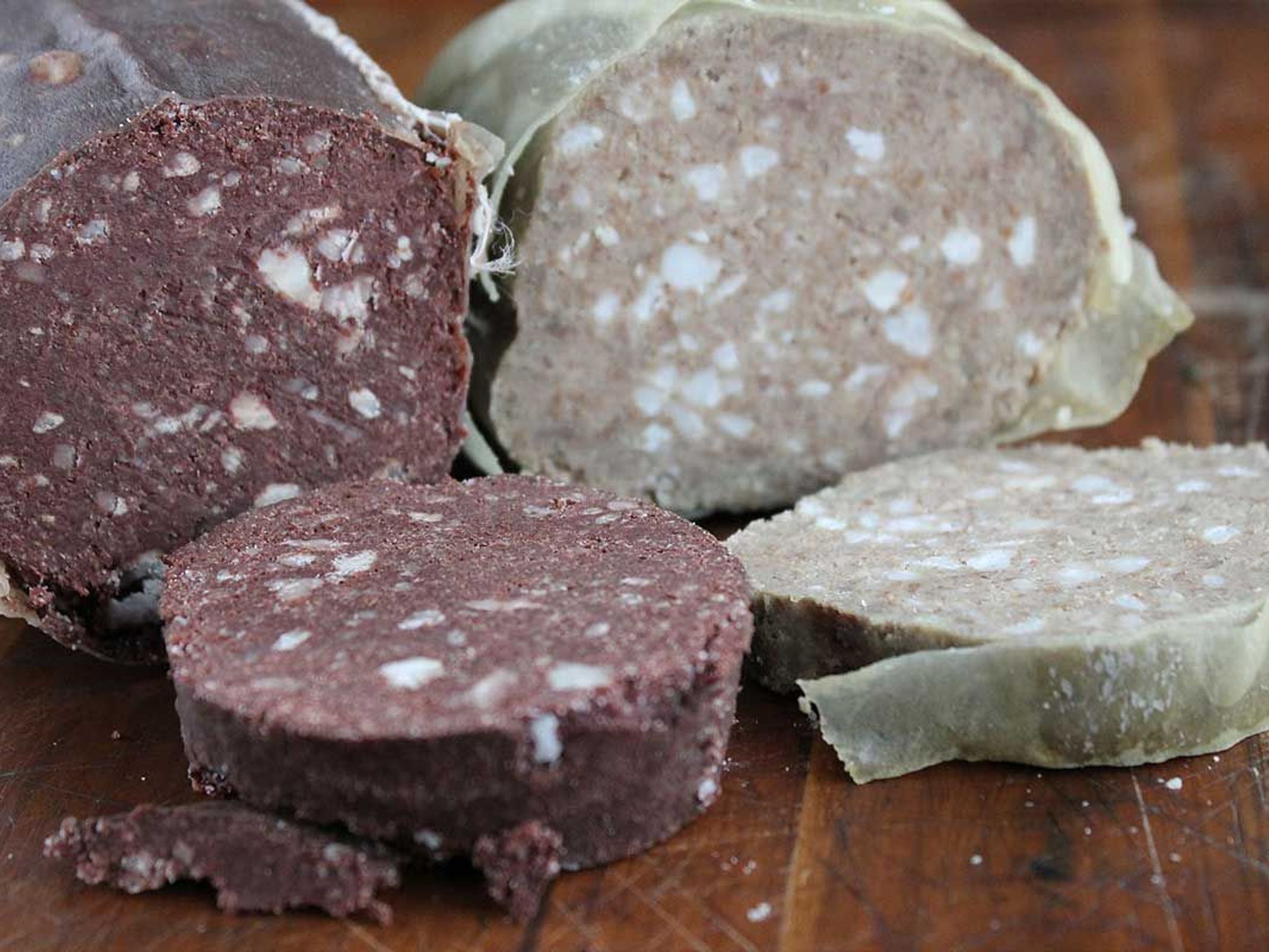Slices of dark blood pudding and light white pudding on a wooden board.