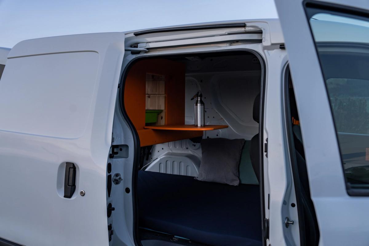 Geöffnete seitliche Schiebetür mit Blick auf das Bett und eine ausklappbare Ablage mit einer Wasserflasche