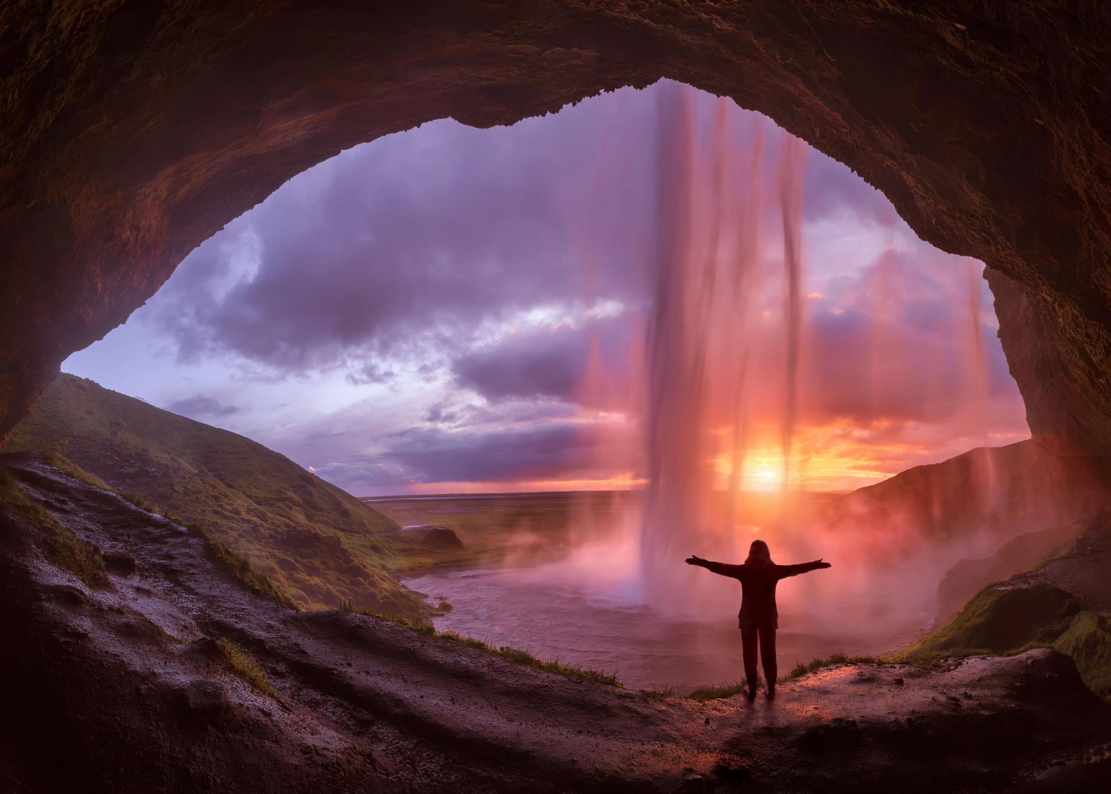 a woman standing behind a waterfall at sunset