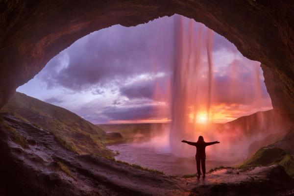 Chica detrás de Seljalandsfoss con el sol a punto de ponerse en el horizonte