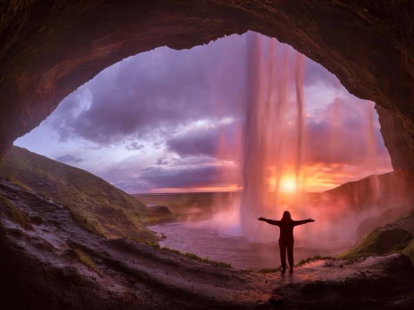 Girl streching her arms behind Seljalandsfoss waterfall during twilight
