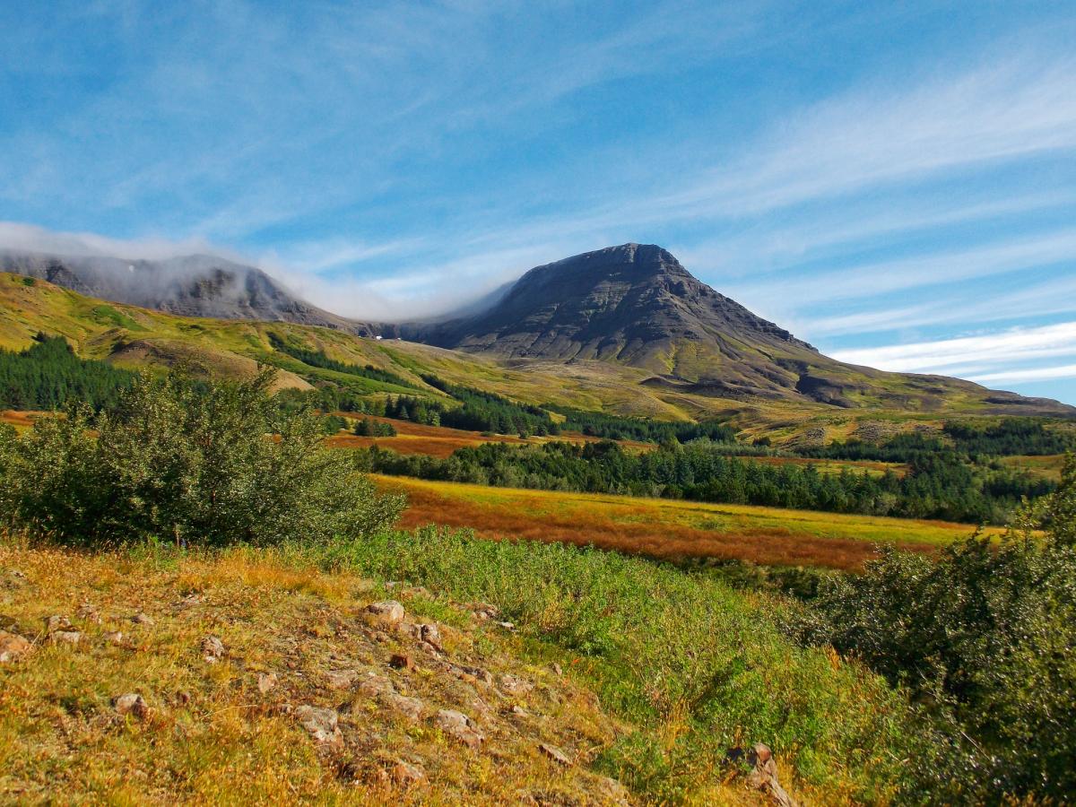 Rugged mountain landscape with colorful fields and low-lying clouds.