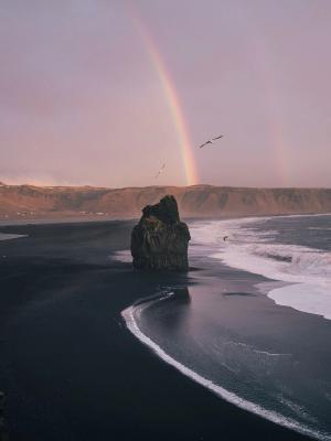Long black sand beach with a massive rainbow in Iceland