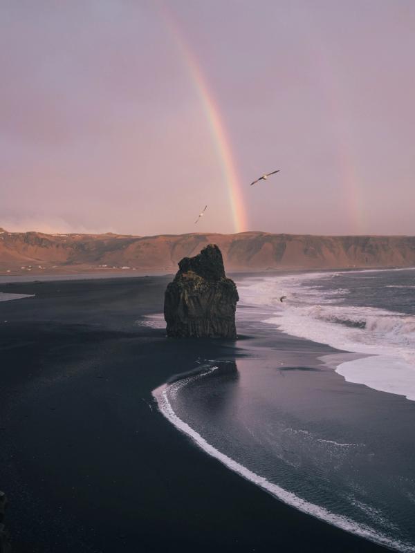 Long black sand beach with a massive rainbow in Iceland