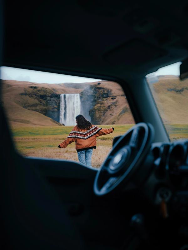 a woman in a sweater is standing in front of a waterfall