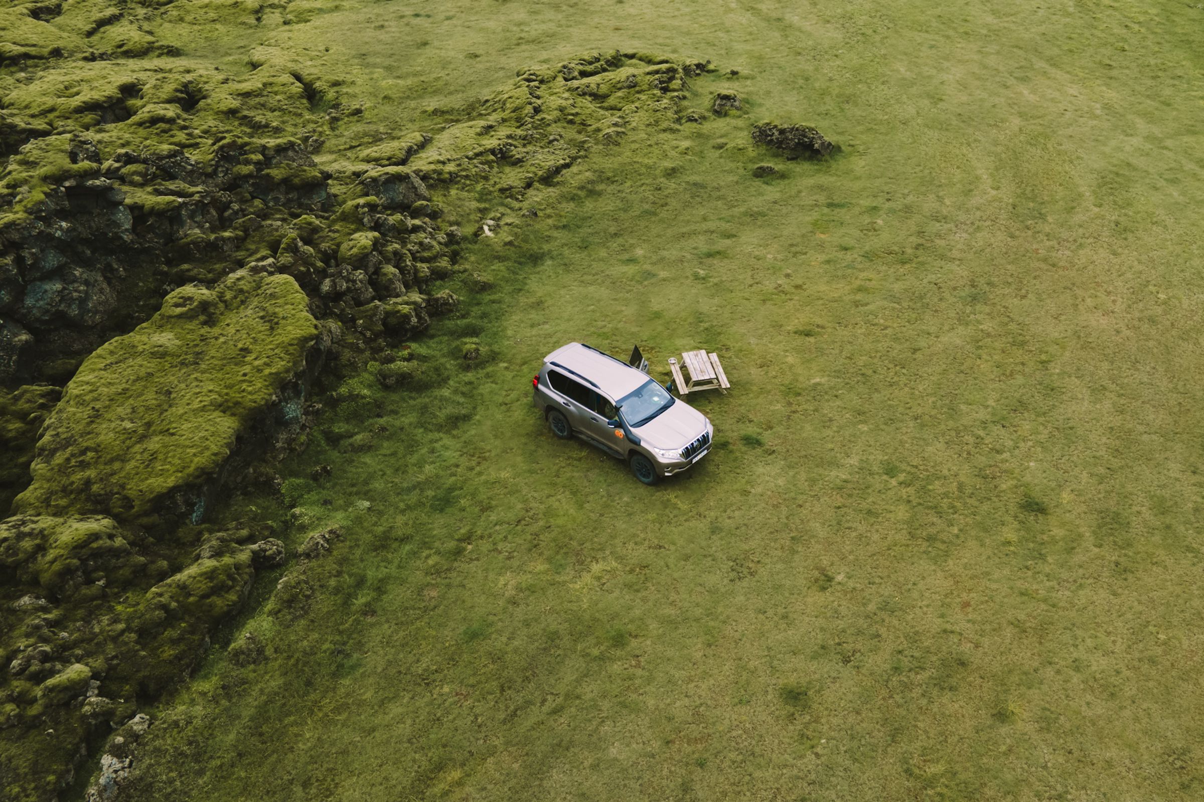 Loftmynd af 4x4 húsbíl við hliðina á lautarborði á grasflöt nálægt mosavöxnum klettum