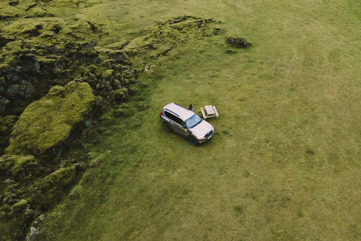 Loftmynd af 4x4 húsbíl við hliðina á lautarborði á grasflöt nálægt mosavöxnum klettum