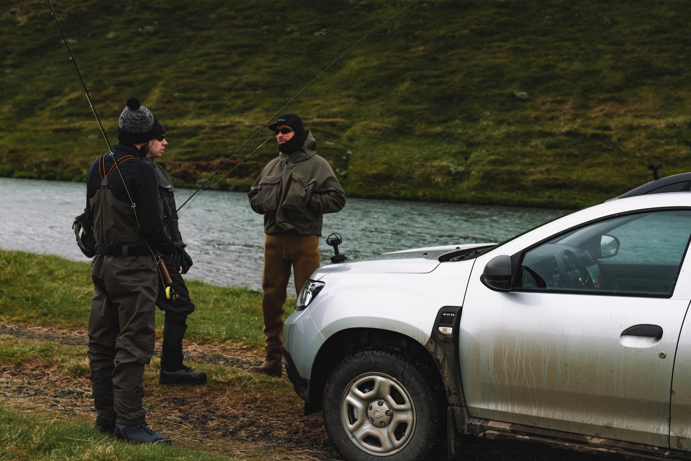 Dacia Duster 4x4 rental Iceland parked riverside with two people holding fishing rods