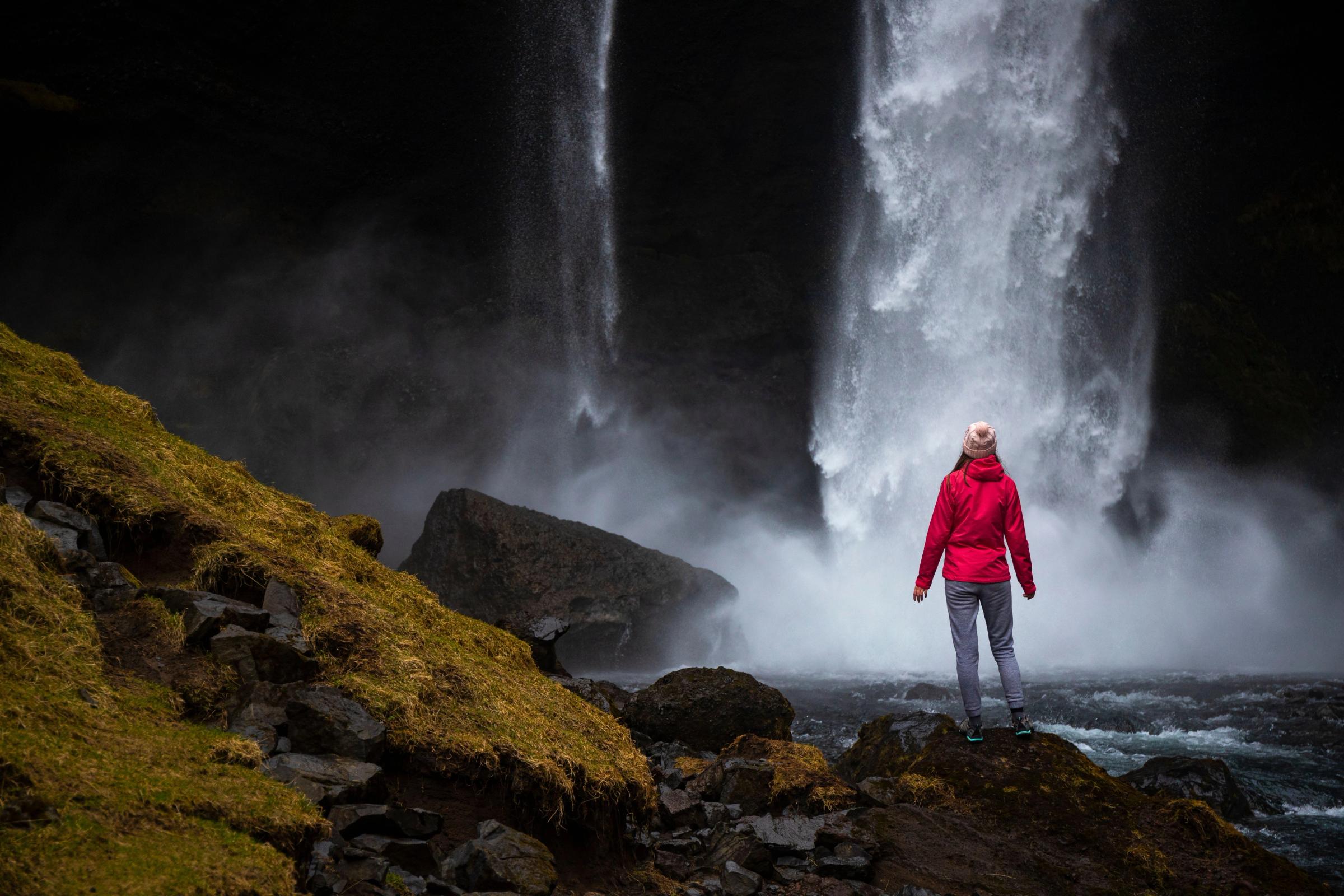a woman in a red jacket is standing in front of a waterfall .