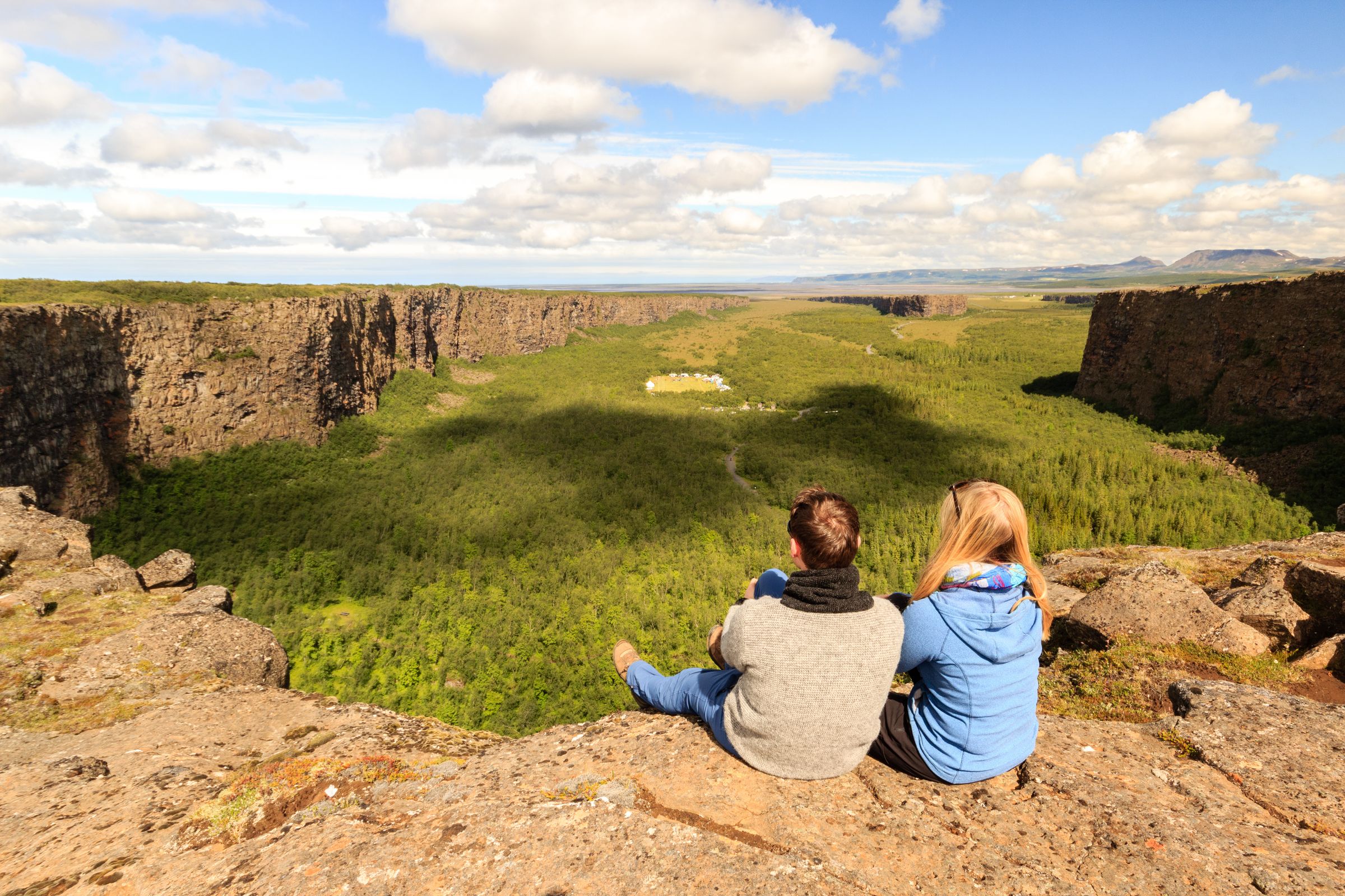 un hombre y una mujer están sentados en la cima de una roca contemplando un valle .
