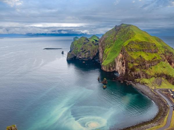a small black sand beach with a green cliff at the end