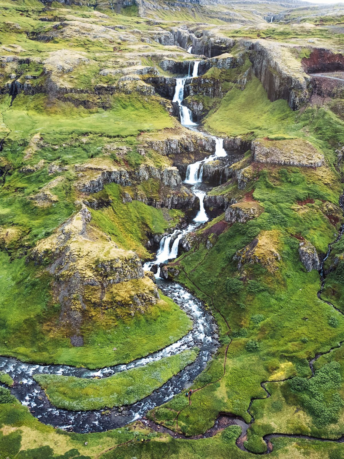 an aerial view of a waterfall in the middle of a lush green valley in klifbrekkufossar in iceland.