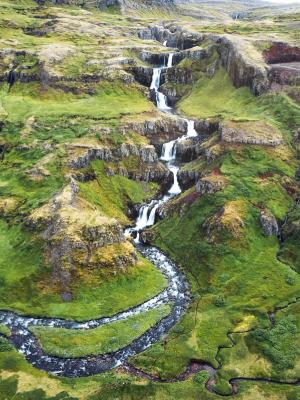 an aerial view of a waterfall in the middle of a lush green valley in klifbrekkufossar in iceland.