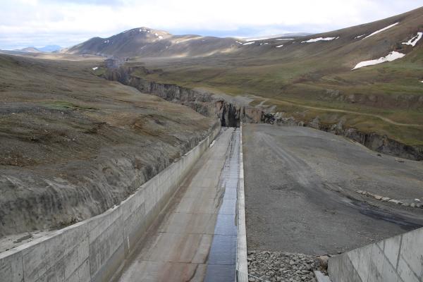A concrete channel leads into a deep, rocky canyon in a rugged landscape with distant hills and snow.