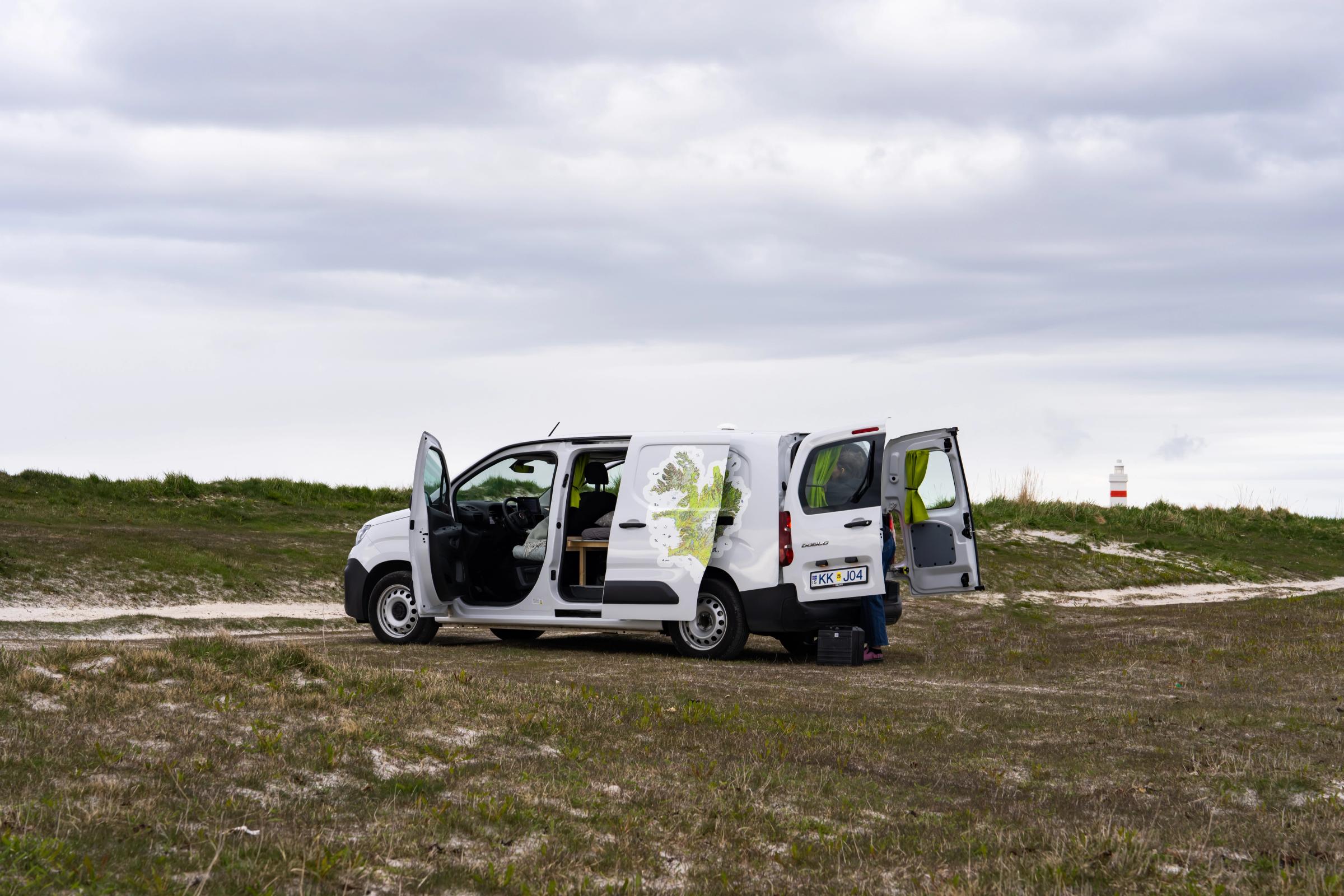 Una autocaravana compacta con capacidad para 2 personas, con las puertas trasera y lateral abiertas, alquiler de autocaravanas en Islandia