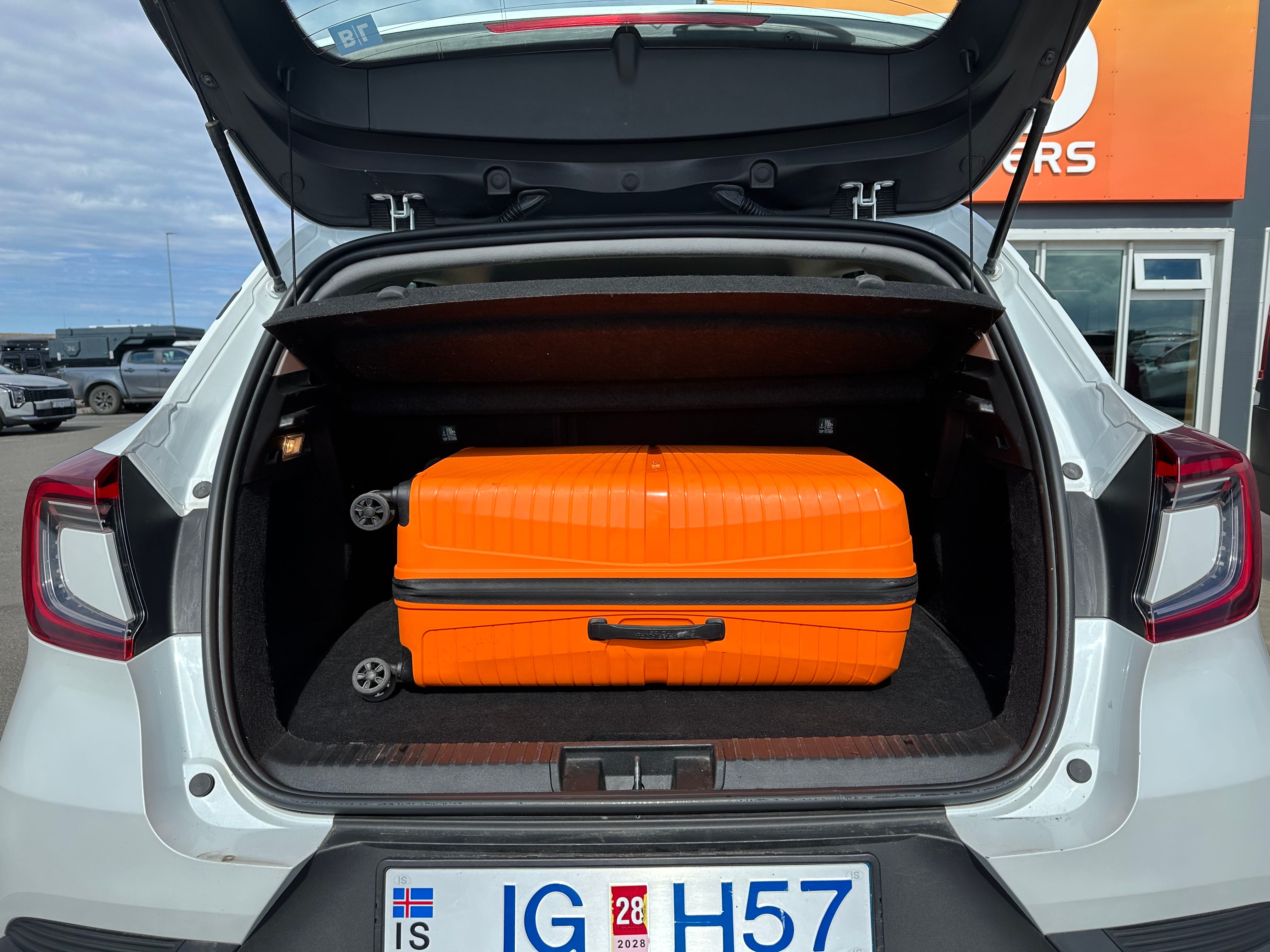 A bright orange suitcase sits in the open trunk of a white car.