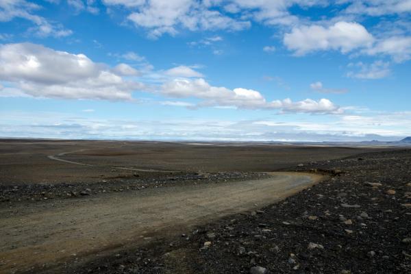 a dirt road in the middle of a desert with a blue sky and clouds in the highlands in iceland.
