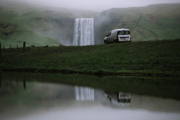 a white van is parked in front of a waterfall next to a lake .