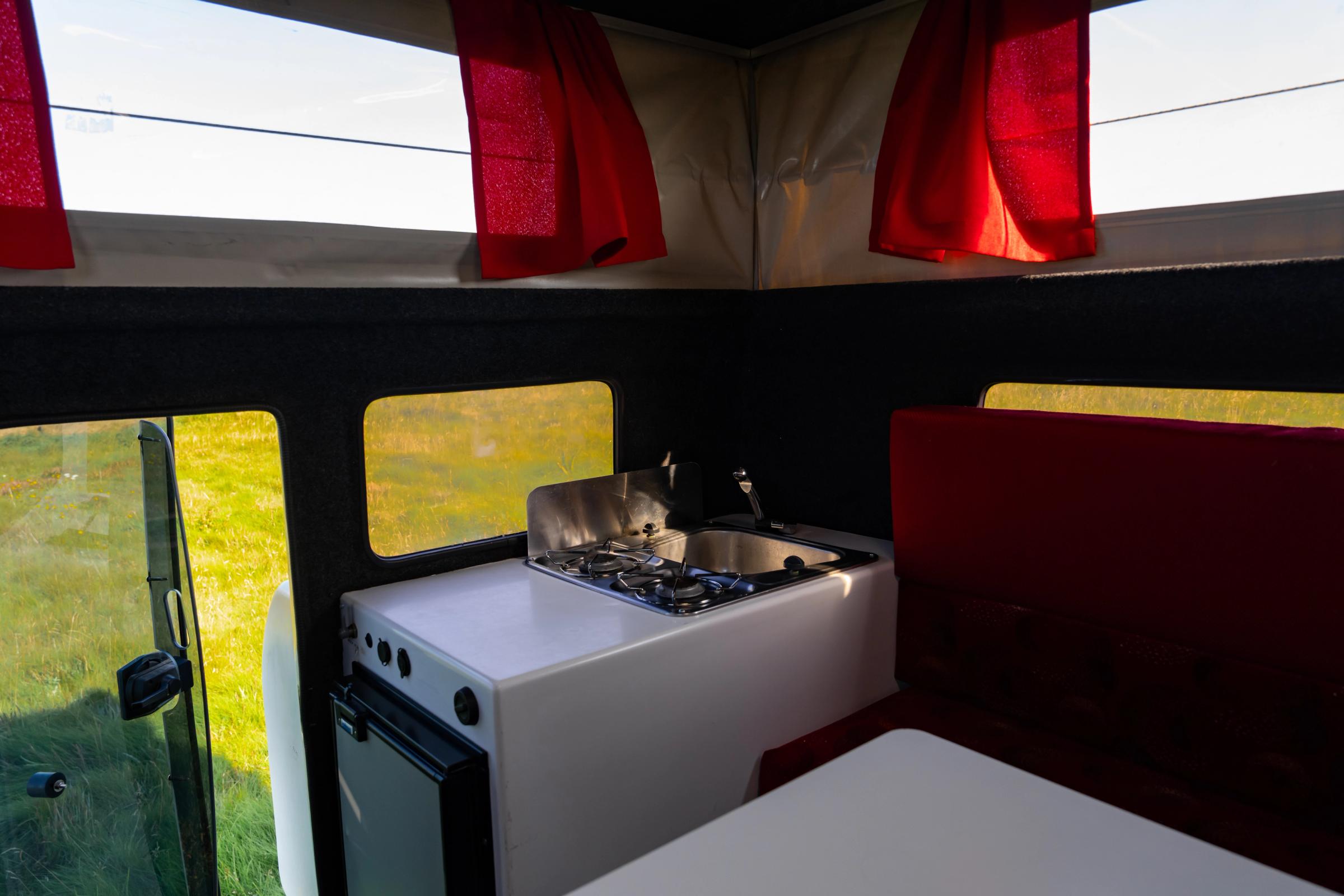 Kitchen Unit Side Angle Kitchen unit with stove, sink and fridge below, next to a red bench seat