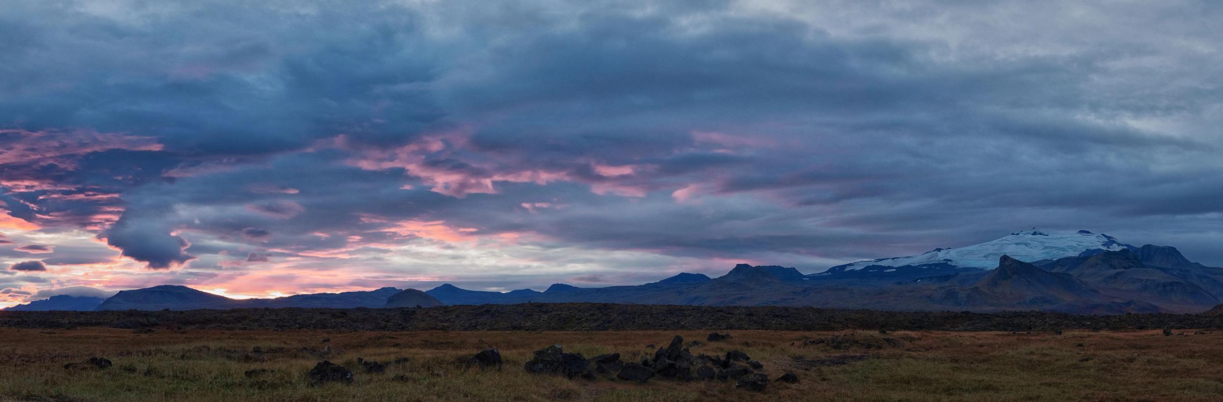 a sunset over a field with mountains in the background