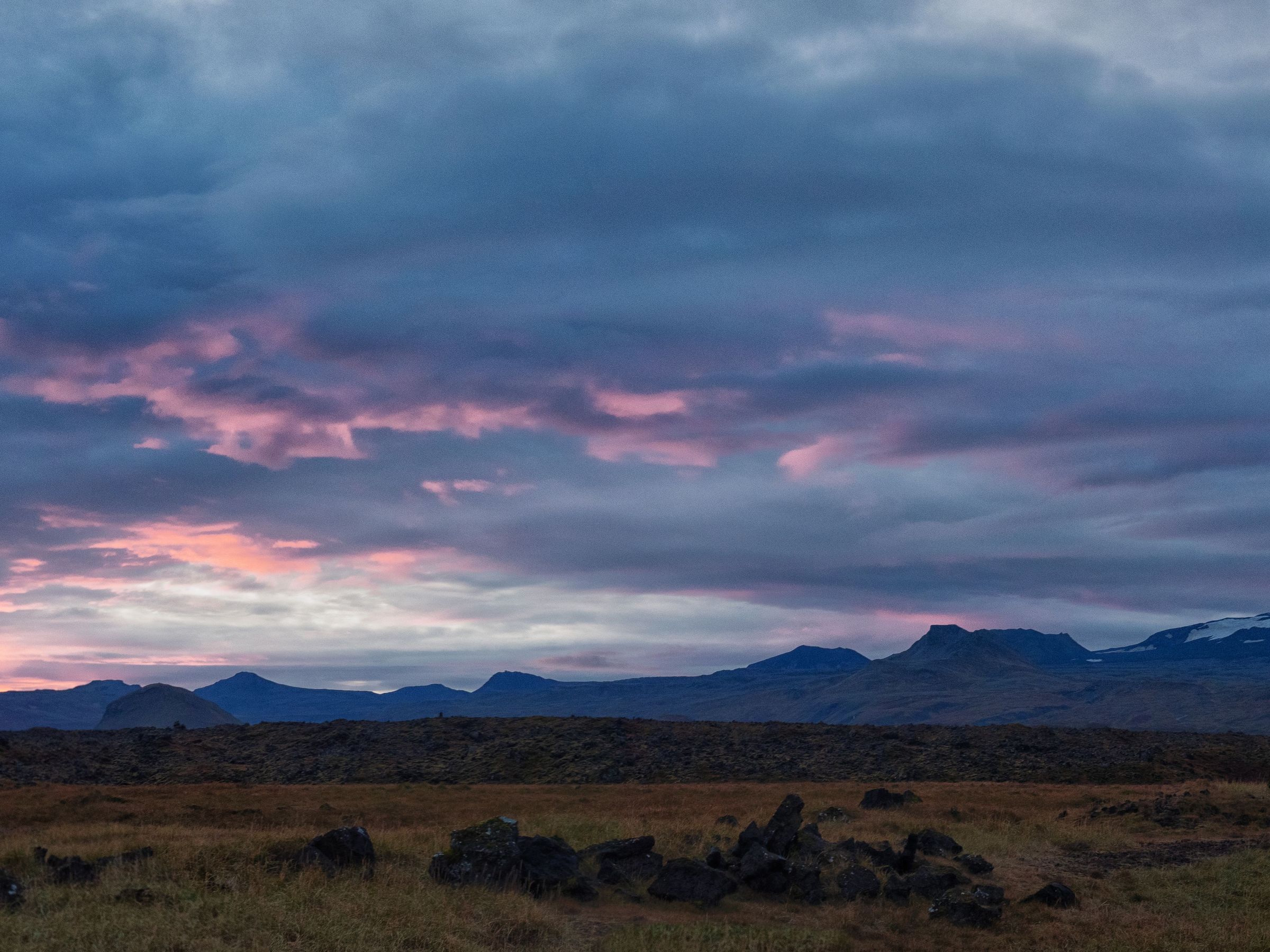 a sunset over a field with mountains in the background