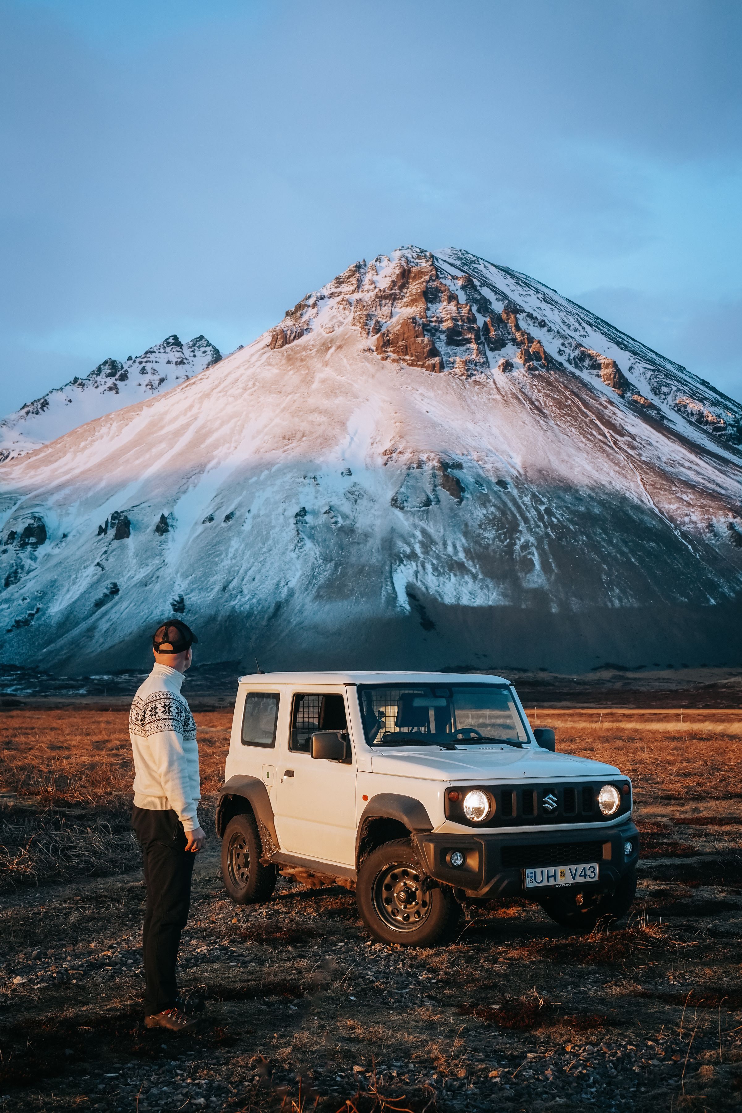Suzuki Jimny automatique garé près des montagnes, avec une personne debout à côté