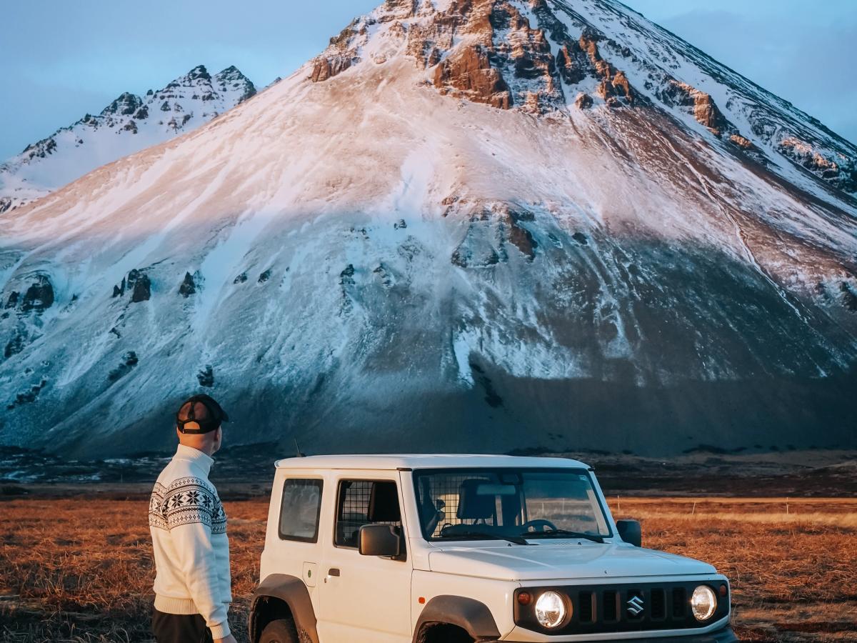 Jimny automatique sur fond de montagnes Suzuki Jimny automatique garé près des montagnes, avec une personne debout à côté