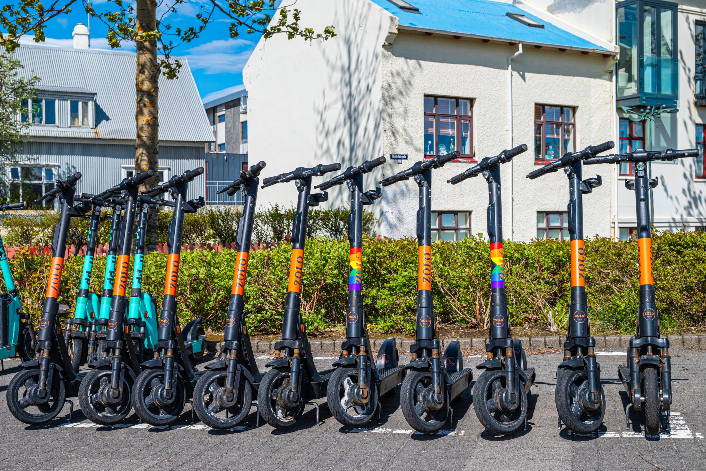 una fila de patinetes eléctricos está aparcada en un estacionamiento frente a un edificio.