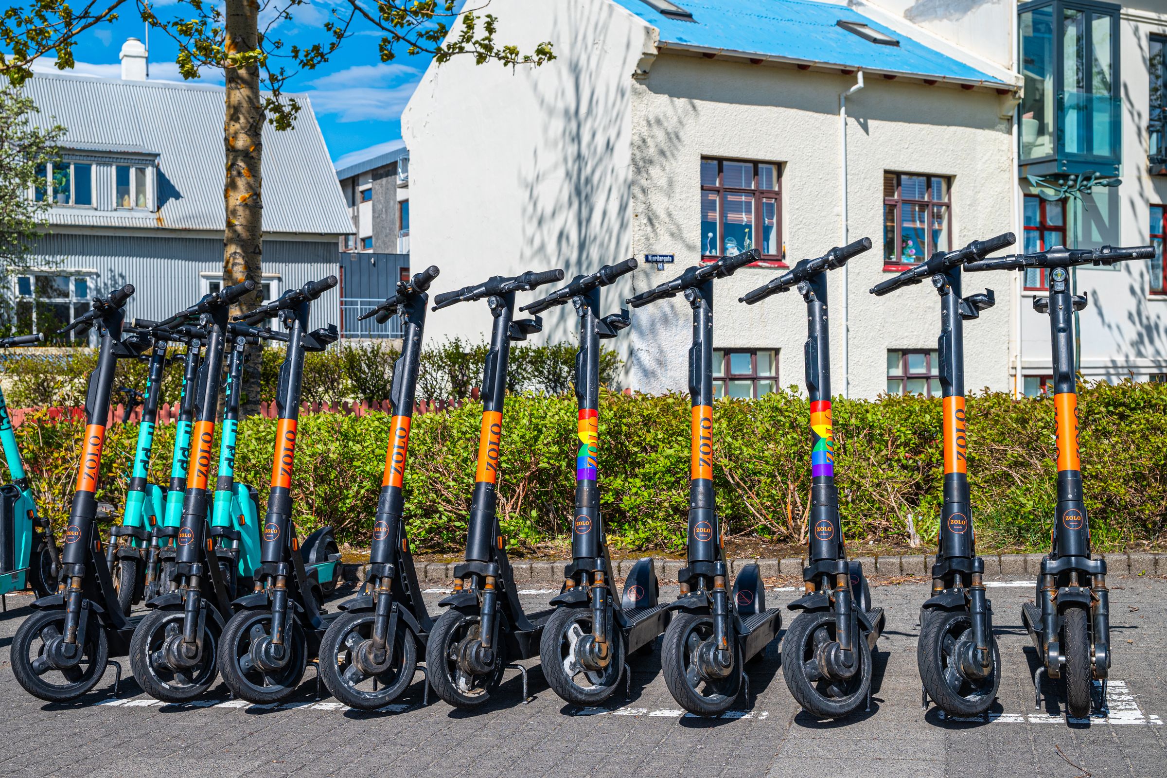 una fila de patinetes eléctricos está aparcada en un estacionamiento frente a un edificio.