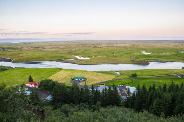 Vista de una enorme llanura verde con un río y algunas casas y árboles