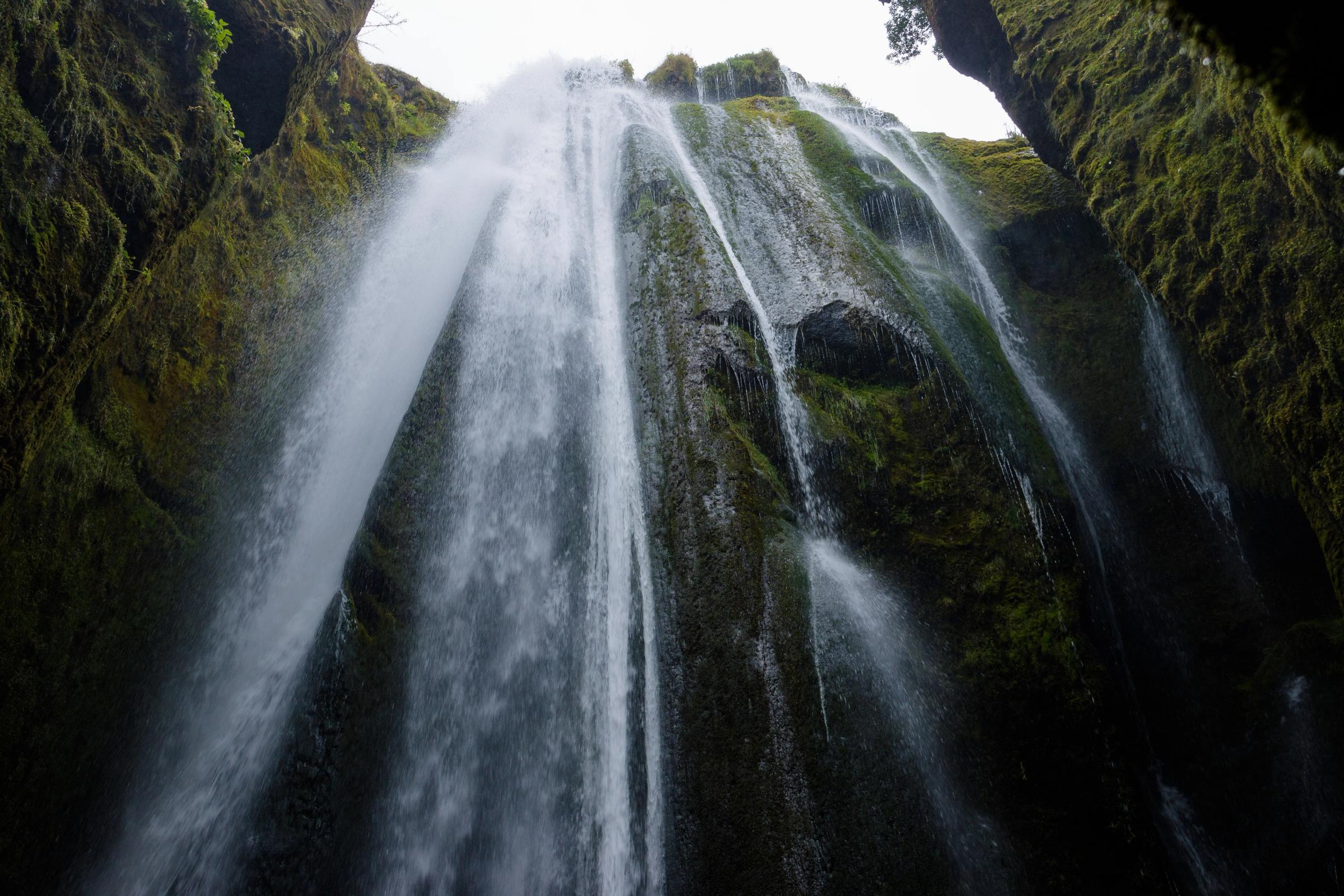 a waterfall is coming down a cliff in the middle of a forest .