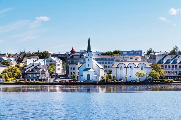a white church with a green steeple is sitting next to a body of water in Reykjavík, iceland.