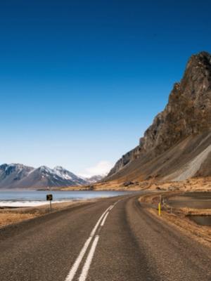 a road going through a mountainous area with a lake and mountains in the background .