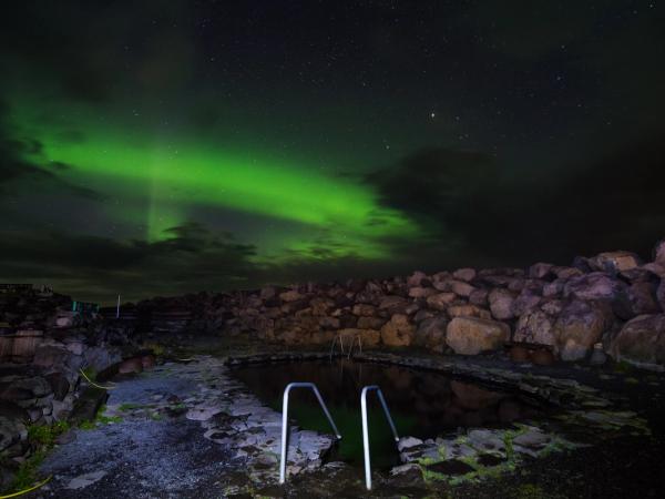 Grettislaug hot spring under the northern lights in North Iceland, surrounded by rugged rocks and night sky.