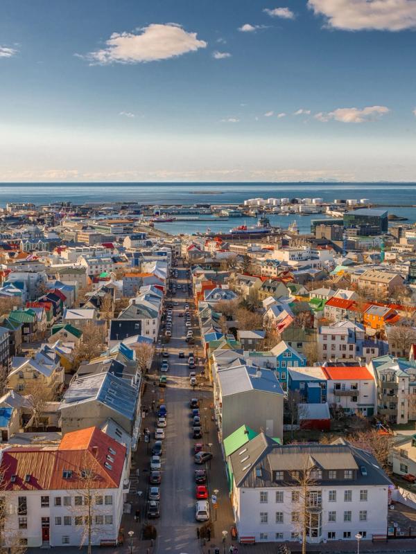 Aerial view of Reykjavik, Iceland, with colorful buildings along a street leading to a bay and distant mountains.