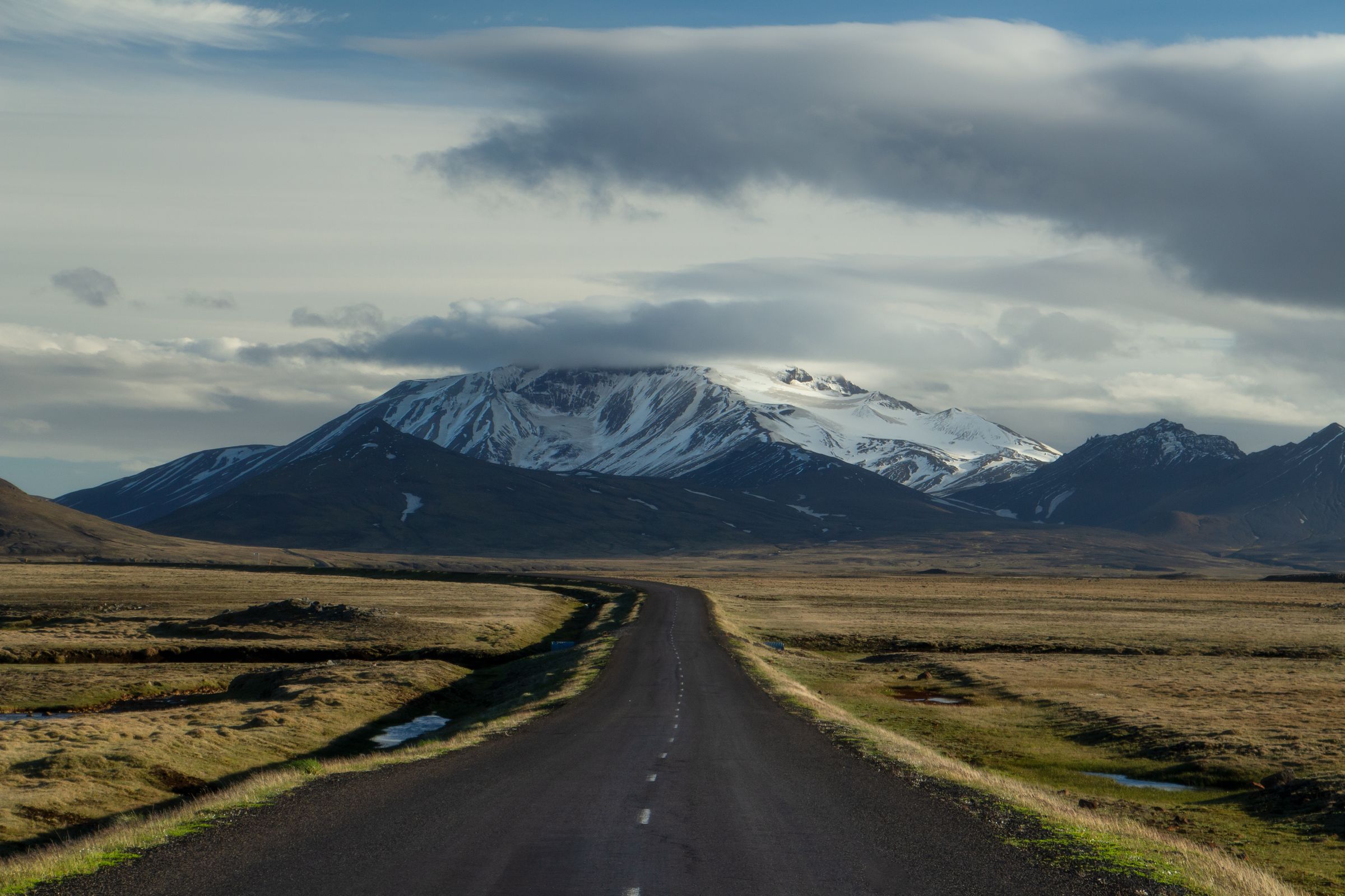 une route traversant un champ avec la montagne Snæfell en arrière-plan.