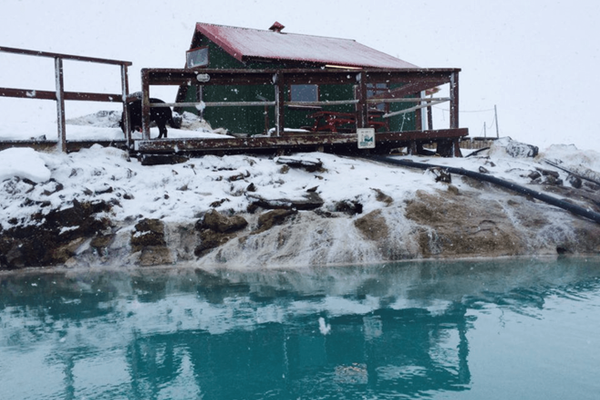 a green house with a red roof sits next to a body of water at hveravellir in iceland.