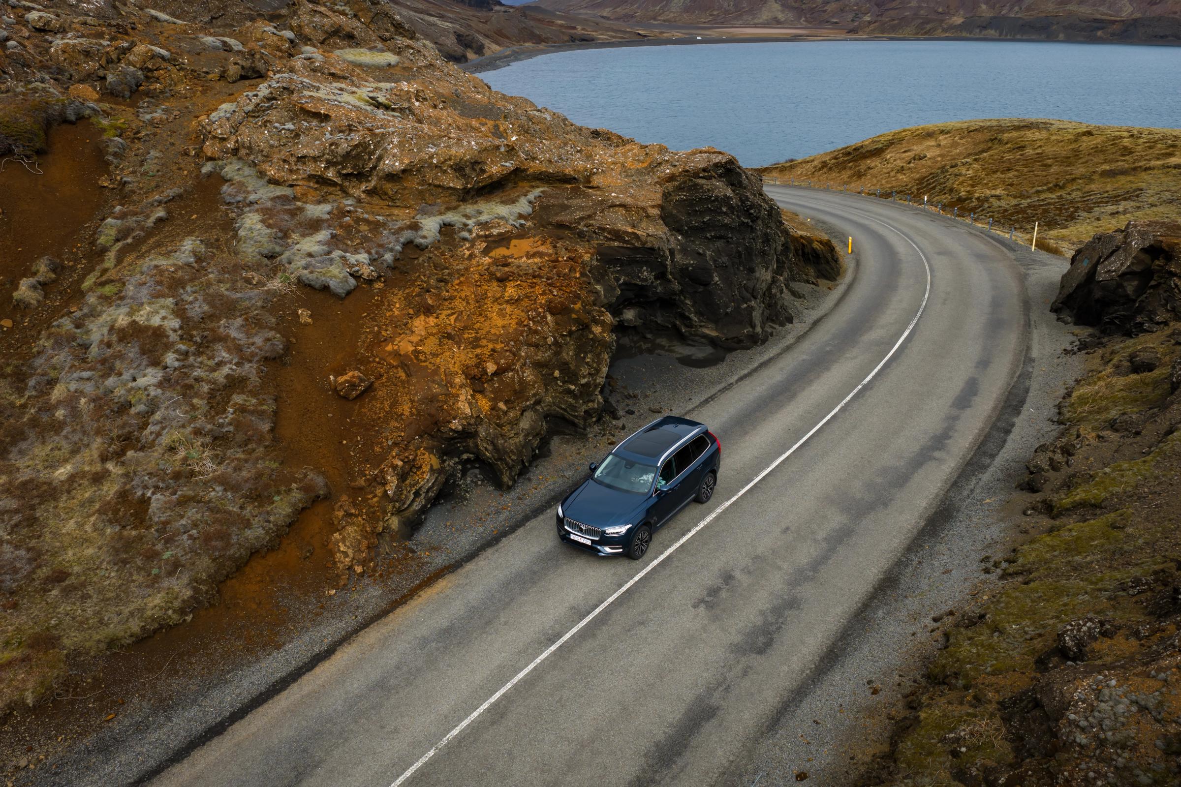 SUV azul en una carretera sinuosa que atraviesa un paisaje rocoso junto a un lago.