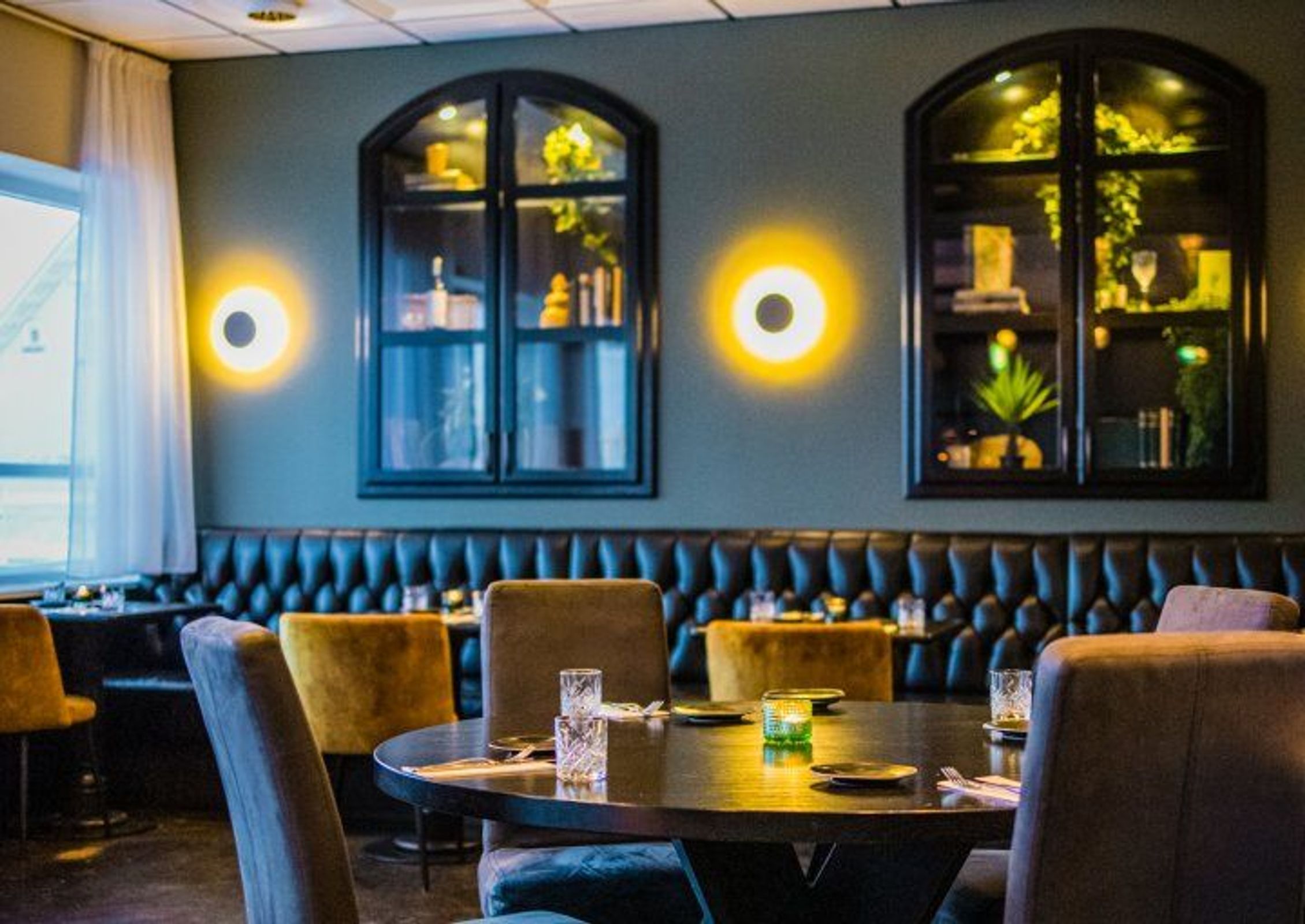 Lit restaurant room where you can see beautiful round tables, cozy space