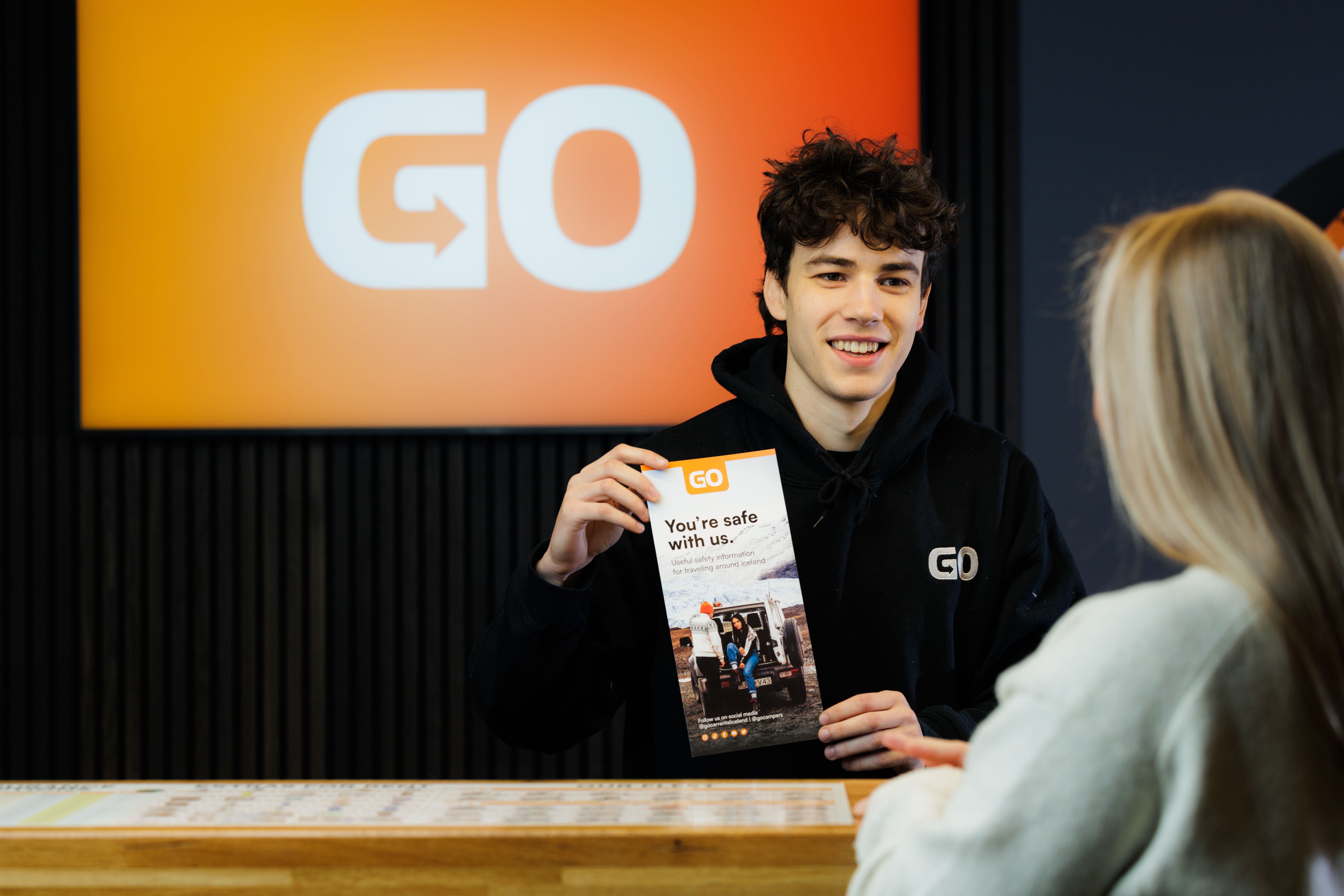 a man is holding a pamphlet in front of a woman at a counter .