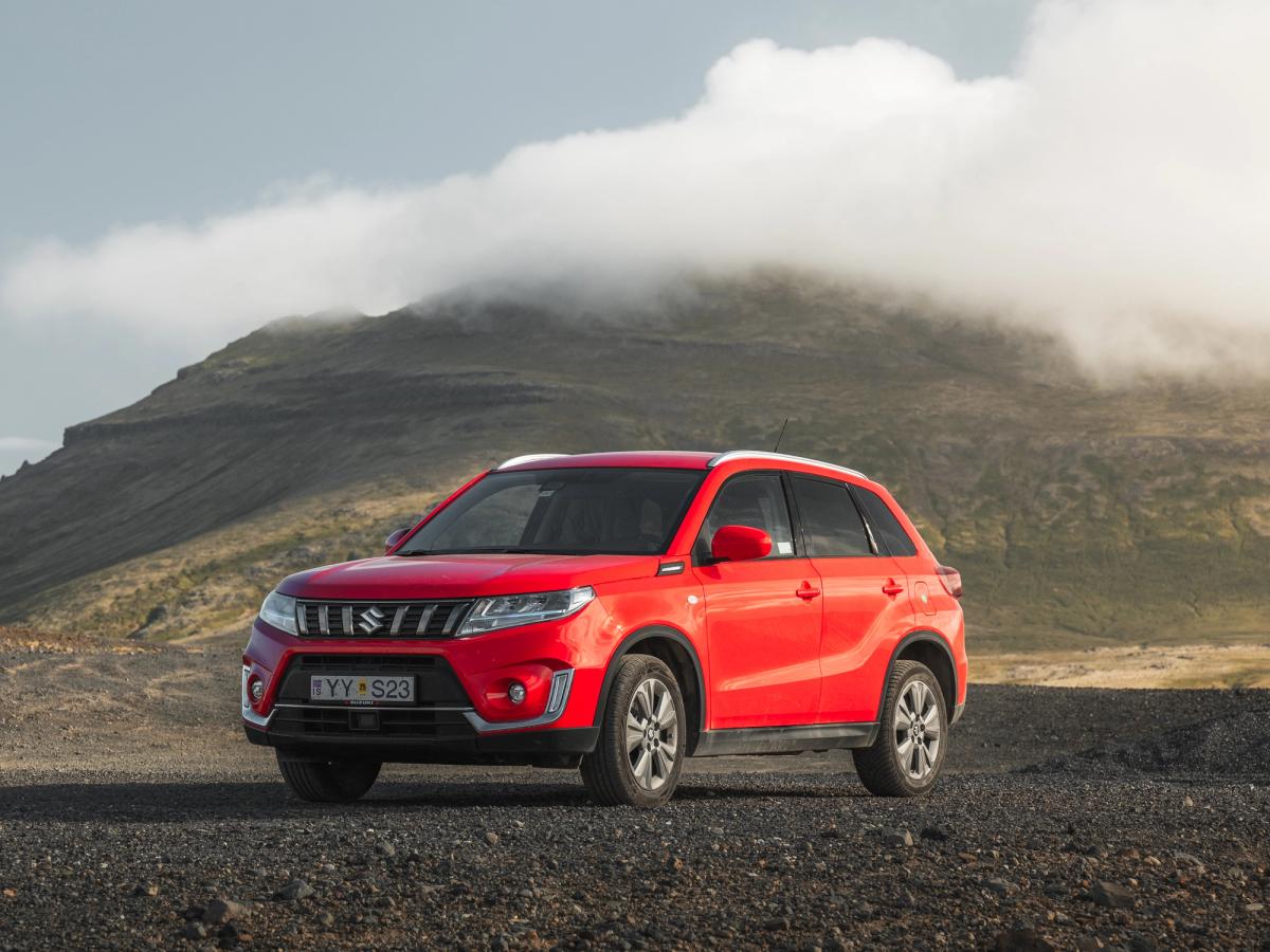 Vitara vue de face en angle avec nuages Vue de trois quarts avant d’un SUV Suzuki Vitara garé sur du gravier, avec des nuages bas au-dessus d’une montagne