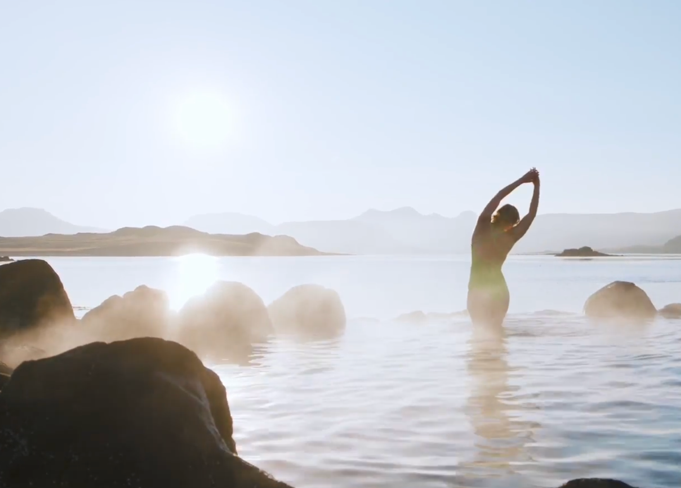 Mujer estirándose en una fuente termal humeante al atardecer.