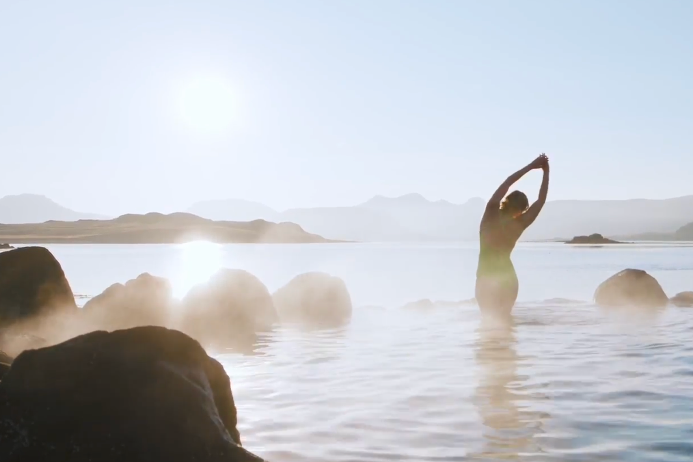 Mujer estirándose en una fuente termal humeante al atardecer.